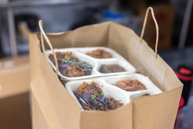 A paper bag containing colorful meals stacked in compartmented trays.